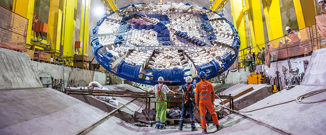 Construction site personnel monitoring the delivery of a blue and white cutting wheel in the tunnel