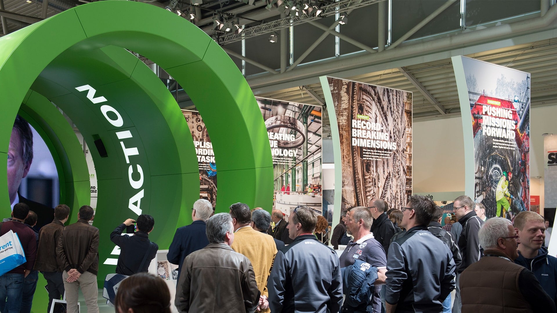 Exhibition booth at bauma 2016 with a crowd of people looking at a green tunnel with high partitions in the background